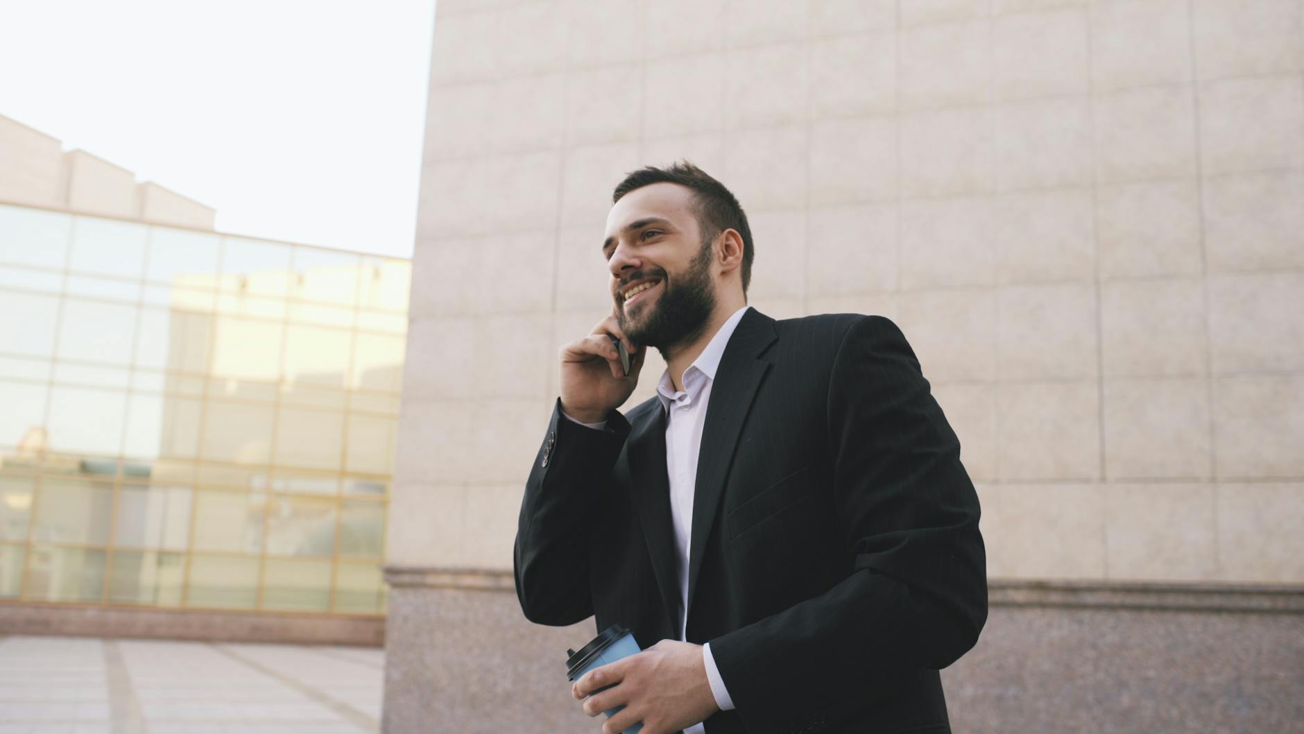 Biznesmen w garniturze rozmawia przez telefon w mieście, trzyma kubek kawy