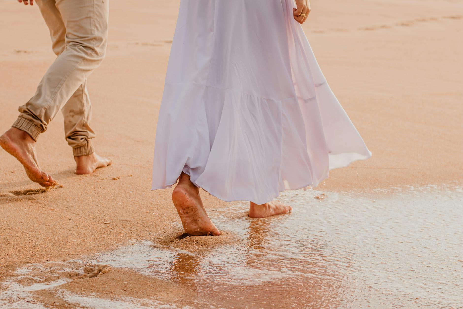 Para spaceruje boso po piaszczystej plaży nad morzem