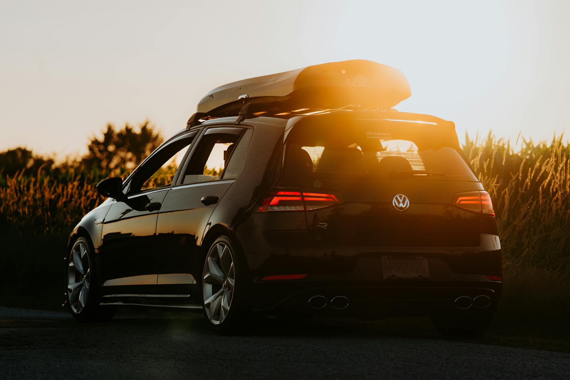 Czarny samochód z boxem dachowym zaparkowany na wiejskiej drodze o zmierzchu