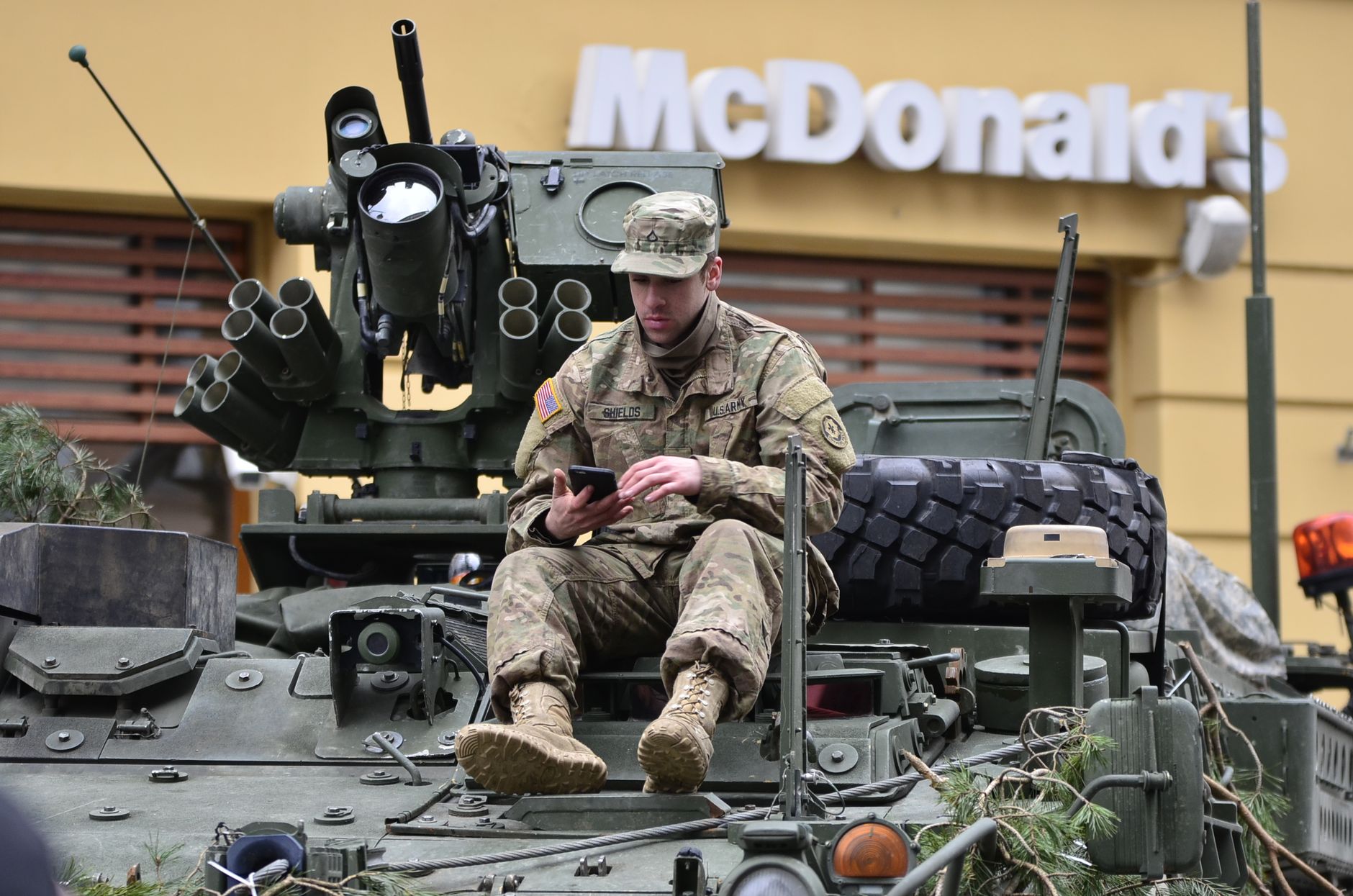 Żołnierz w mundurze korzysta ze smartfona na pojeździe przed McDonald’s