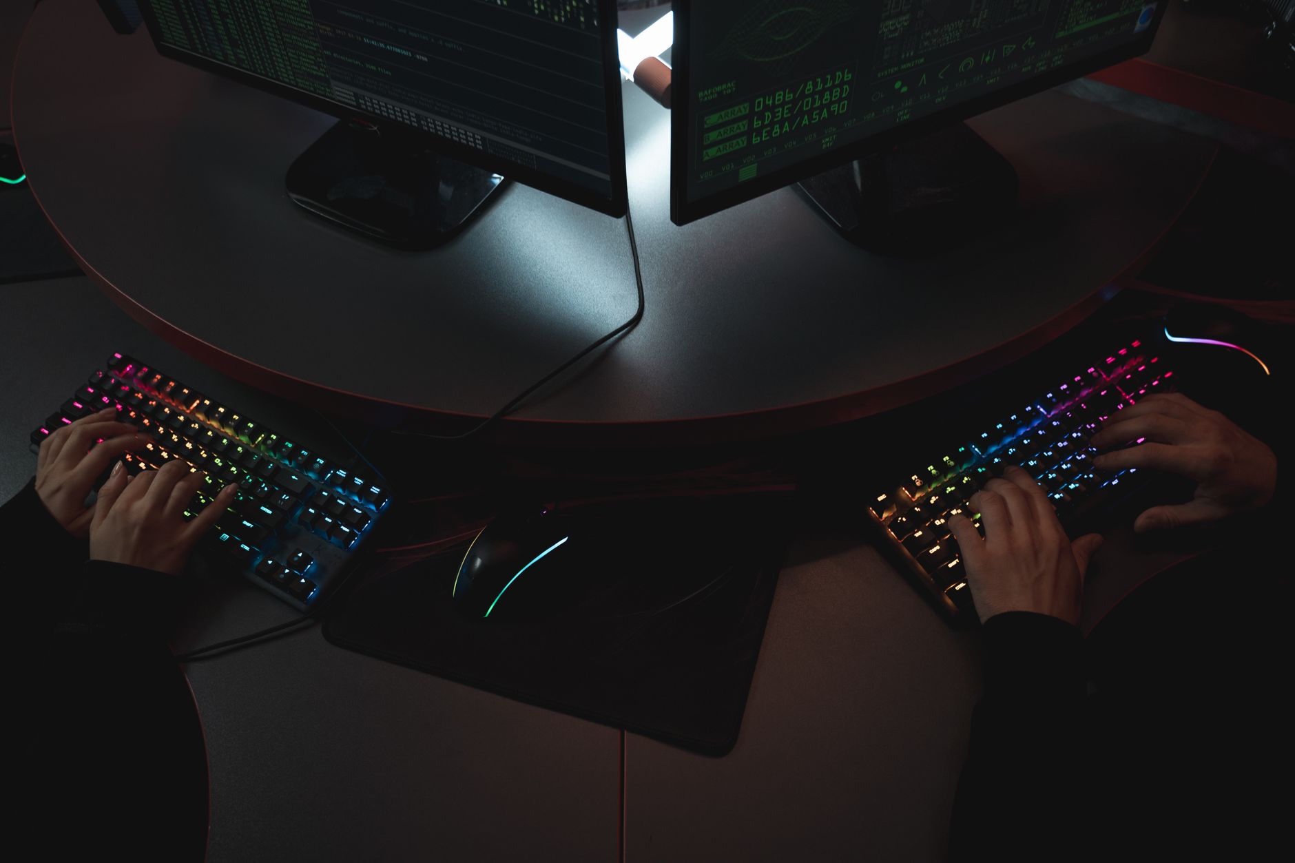 Dwie osoby piszące na klawiaturach RGB przy ekranach z kodem