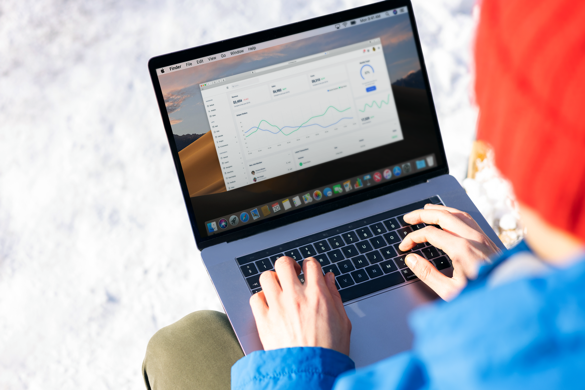 Osoba w niebieskiej kurtce analizuje wykresy KPI DevOps na laptopie zimą