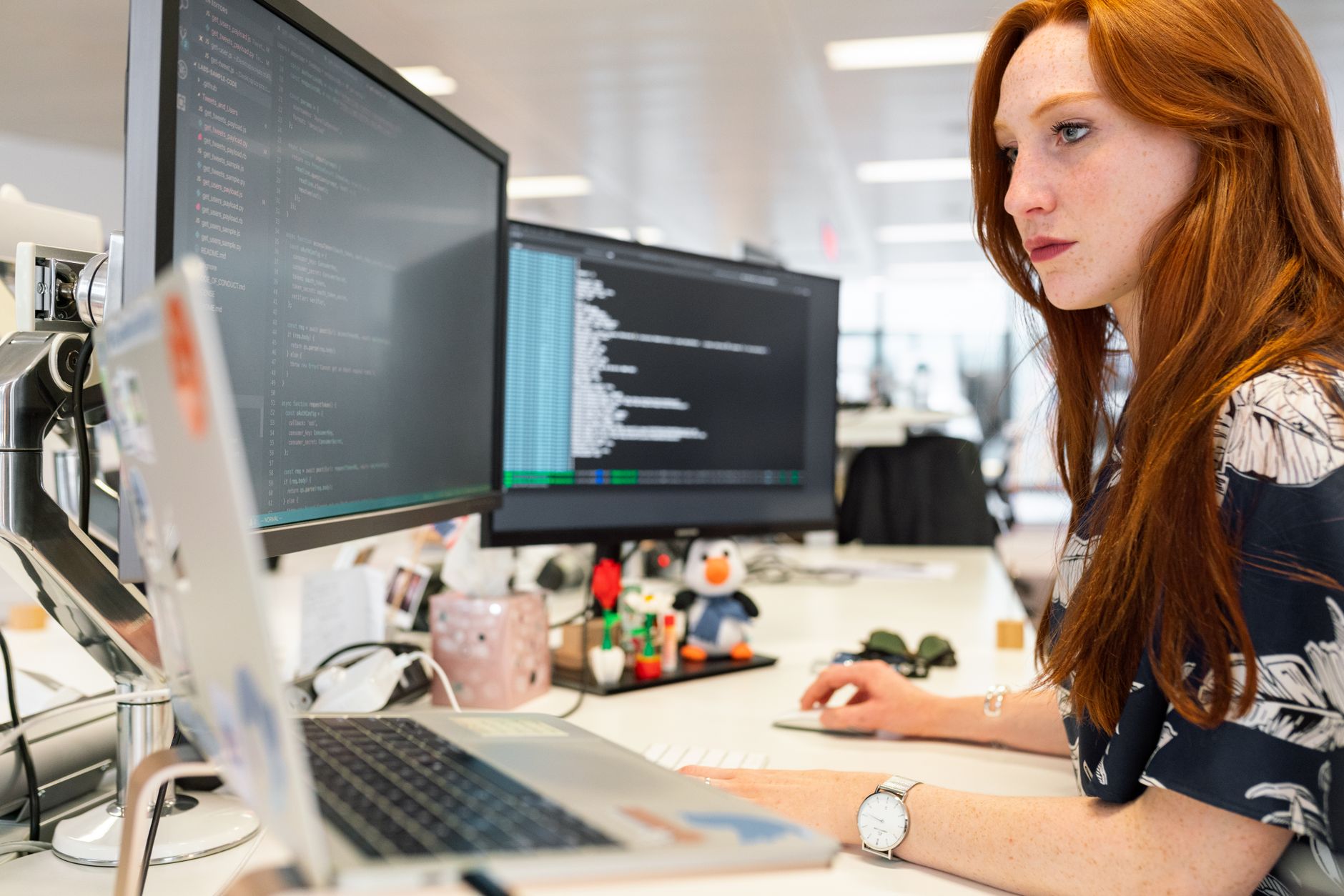 Programistka przy dwóch monitorach pracuje nad kodem w nowoczesnym biurze